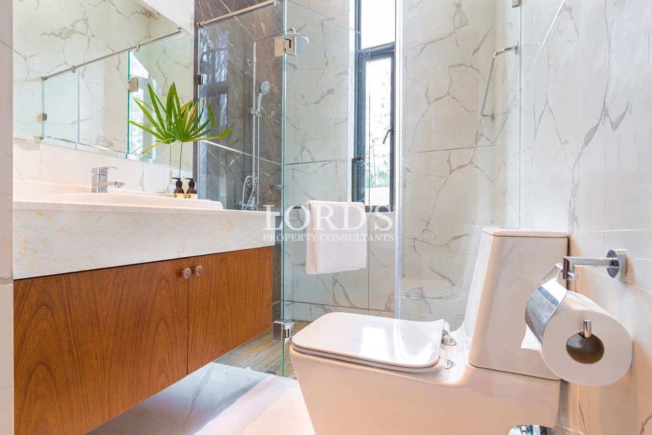 Modern bathroom with walk-in glass shower, wooden vanity, marble-effect tiles, and contemporary toilet.