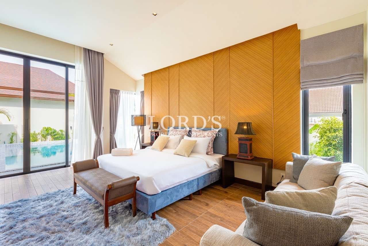Spacious luxury bedroom with king-size bed, wooden accent wall, seating area, and pool view.