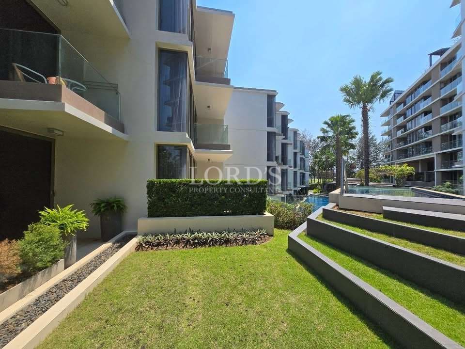 Modern condominium garden courtyard with landscaped lawn, palm trees, and residential buildings.