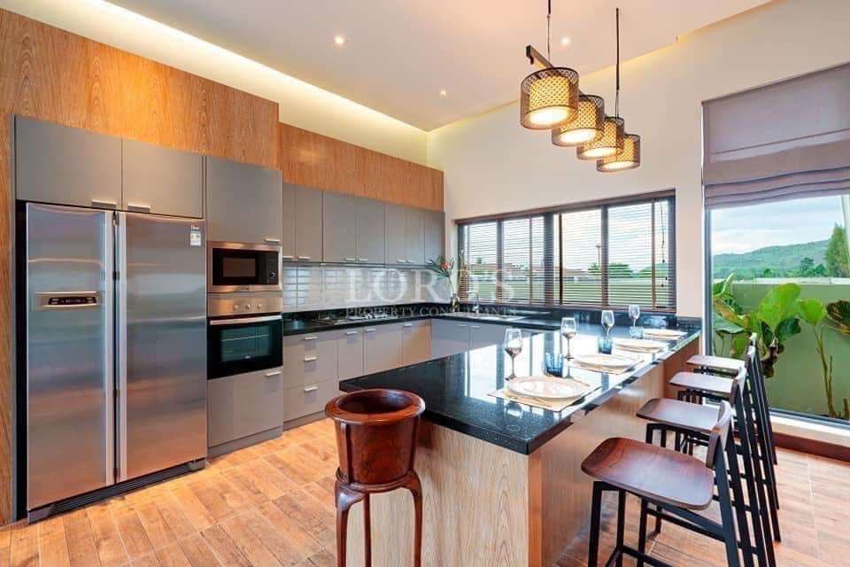 Modern kitchen with island counter, stainless steel appliances, pendant lighting, and large windows.