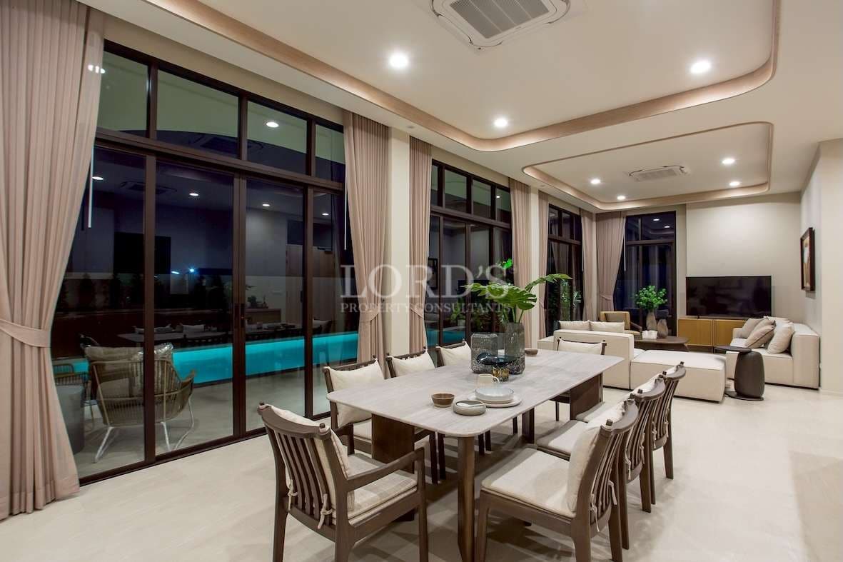 Spacious open-plan living and dining area with large glass doors, modern furniture, and ambient lighting.