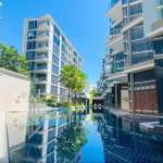 Modern luxury condominium with swimming pool, glass balconies, palm trees, and contemporary architecture.