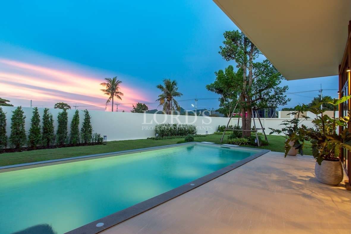 Private swimming pool with landscaped garden and sunset sky at a modern luxury villa.