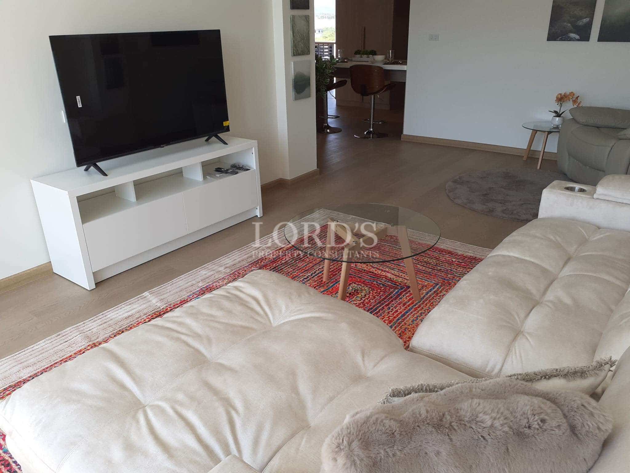 Modern living room with plush sectional sofa, glass coffee table, TV unit, and open-plan dining area