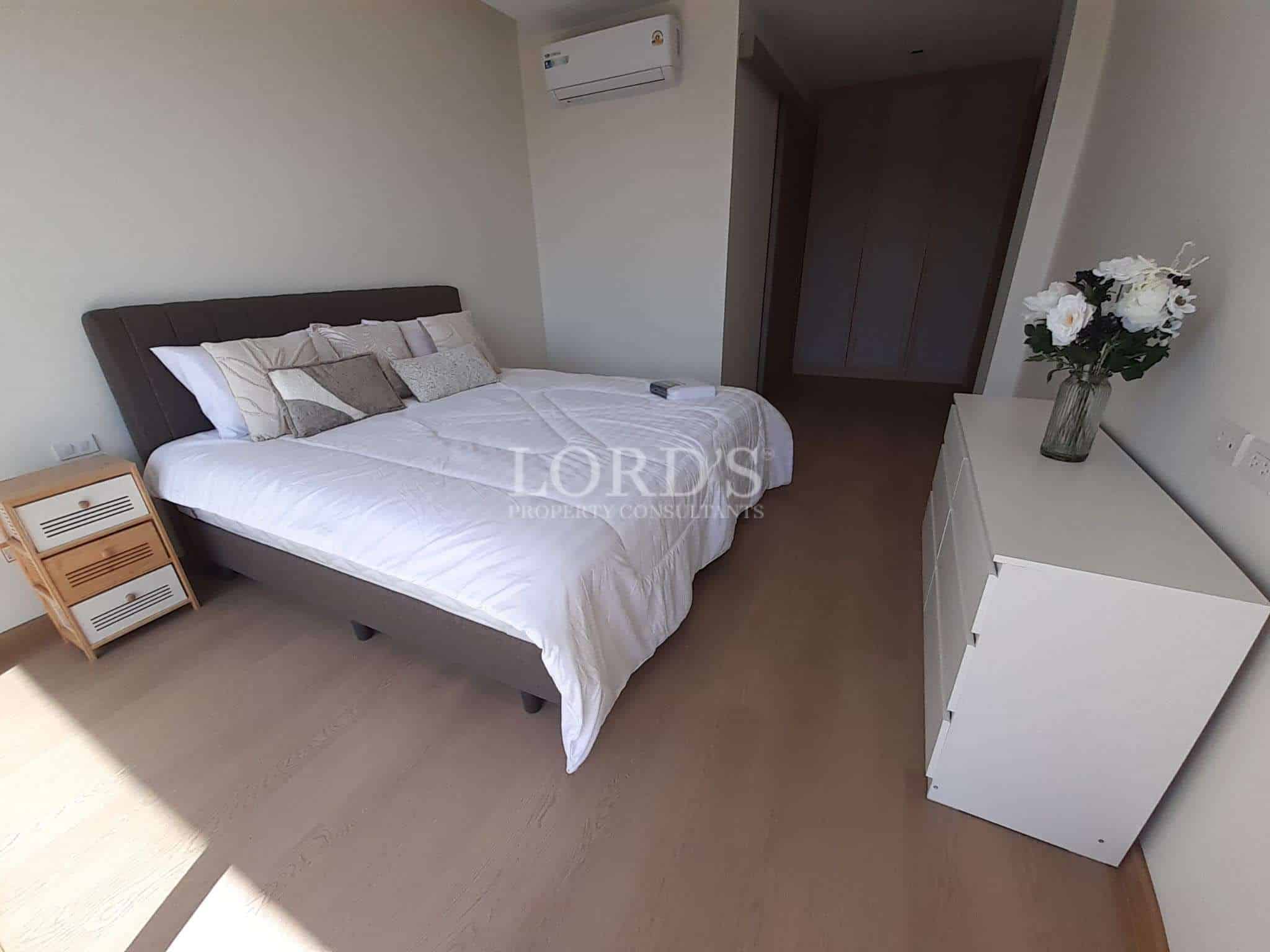 Modern bedroom with double bed, white bedding, wooden floor, air conditioning, and minimalist furniture