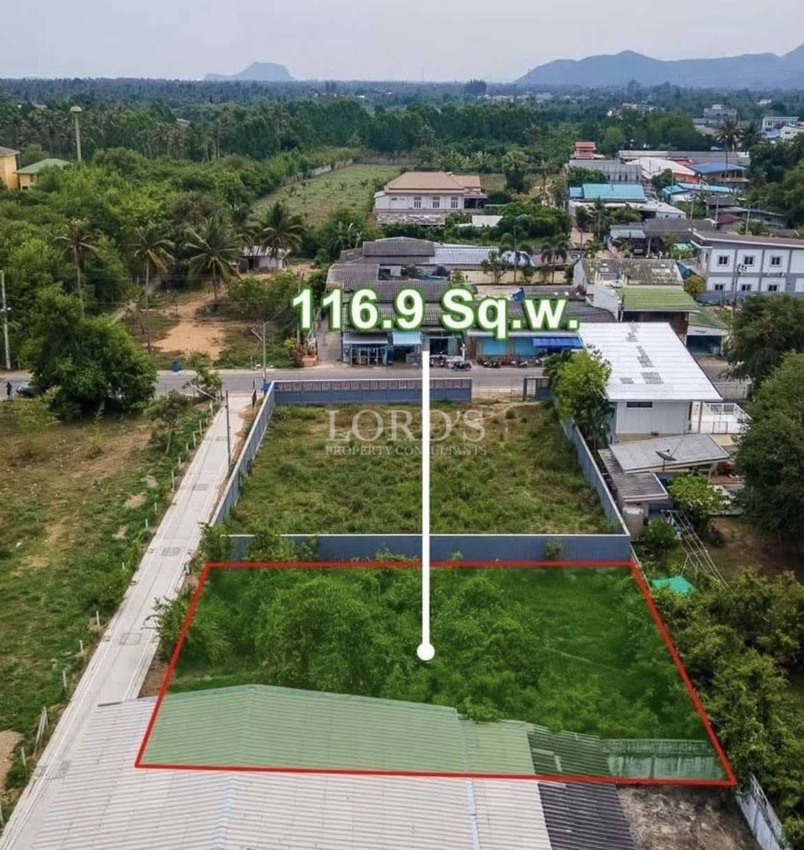 Aerial view of a 116.9 square wah land plot outlined in red, located beside a road with surrounding houses and greenery.