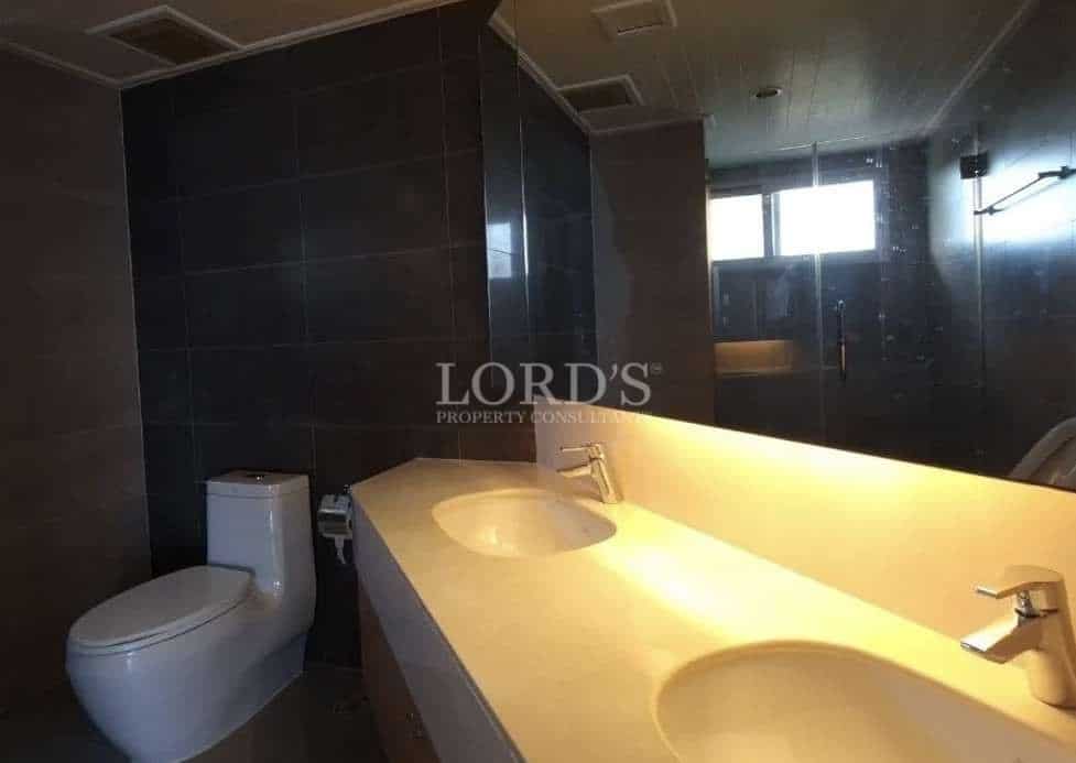 Modern bathroom with double sink vanity, large mirror, toilet, dark tiled walls, and warm lighting.