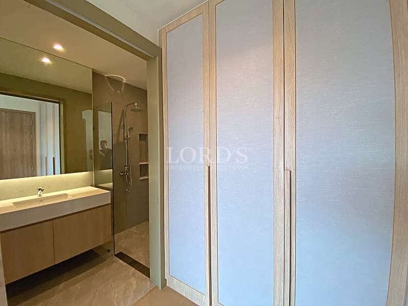 Modern bedroom wardrobe with light wood finish next to a contemporary bathroom featuring a vanity and glass shower.
