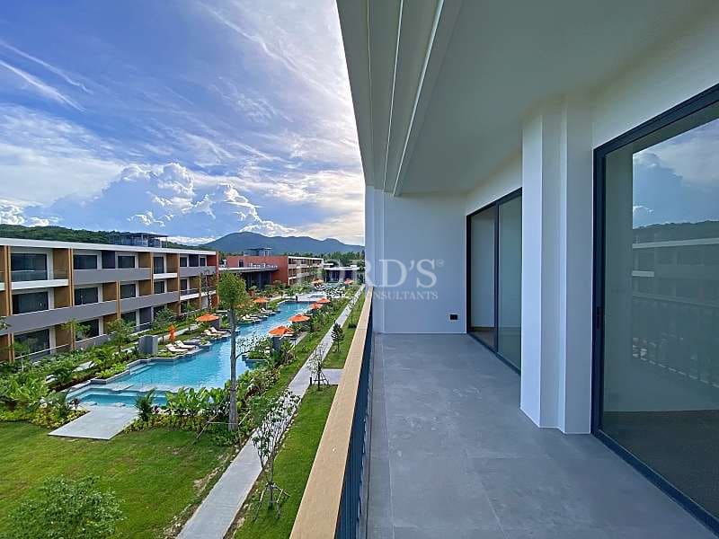 Private apartment balcony overlooking a landscaped courtyard with swimming pool, modern buildings, and mountain views.