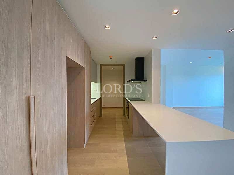Modern minimalist kitchen with light wood cabinetry, built-in storage, and a white island counter in a contemporary apartment.