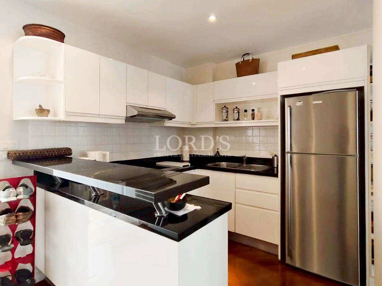 Modern white kitchen with black granite countertops and stainless steel refrigerator.