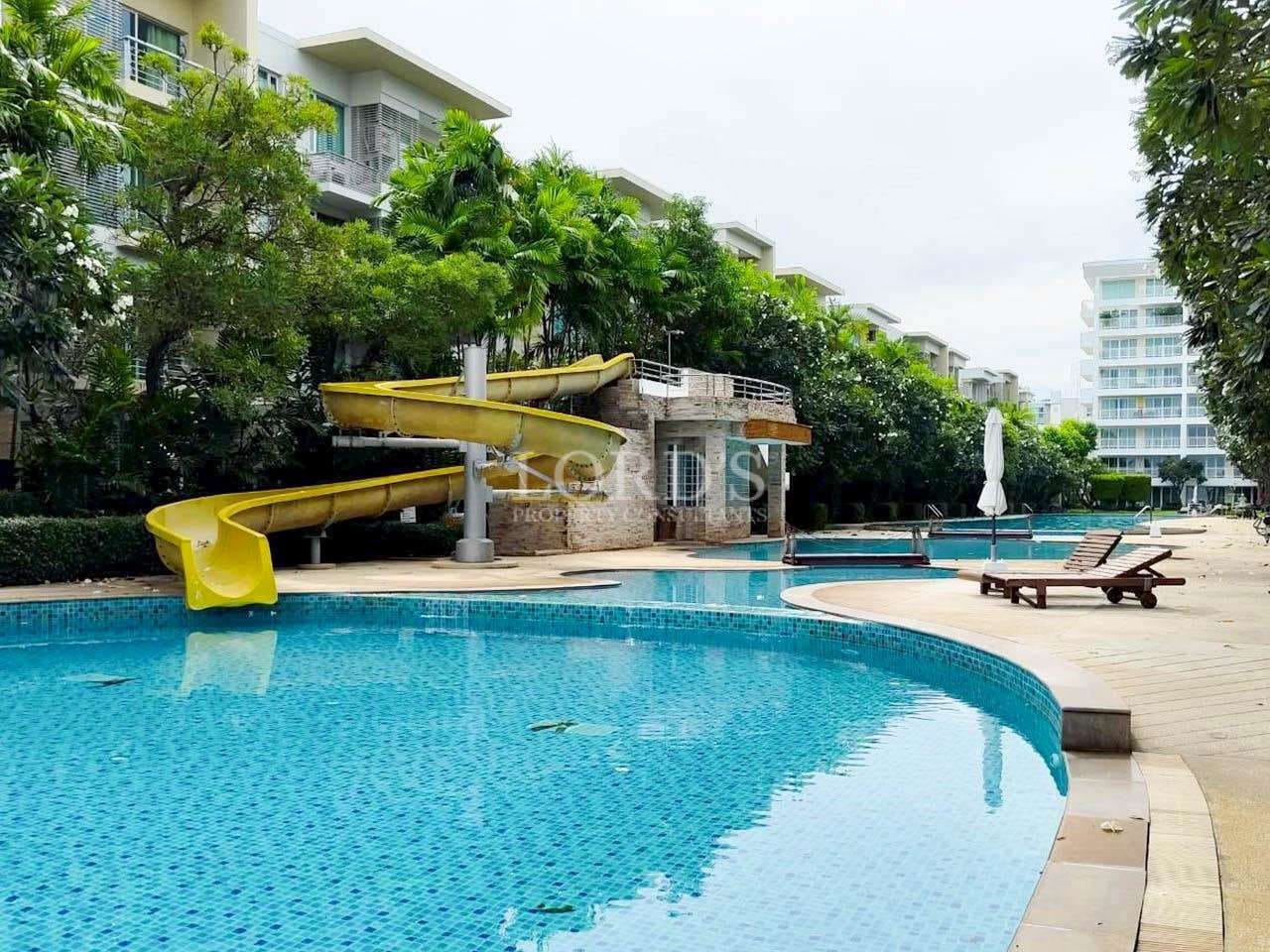 Resort-style swimming pool with water slide surrounded by modern condominium buildings and tropical landscaping.