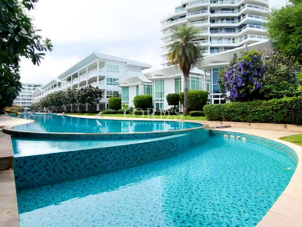 Luxuriöser Swimmingpool in einer Wohnanlage, umgeben von modernen weißen Gebäuden und angelegten Gärten.