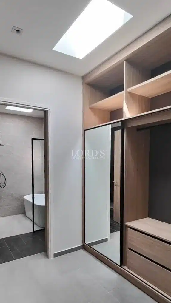 Modern walk-in wardrobe with built-in wooden storage, mirrored sliding doors, skylight, and ensuite bathroom access.