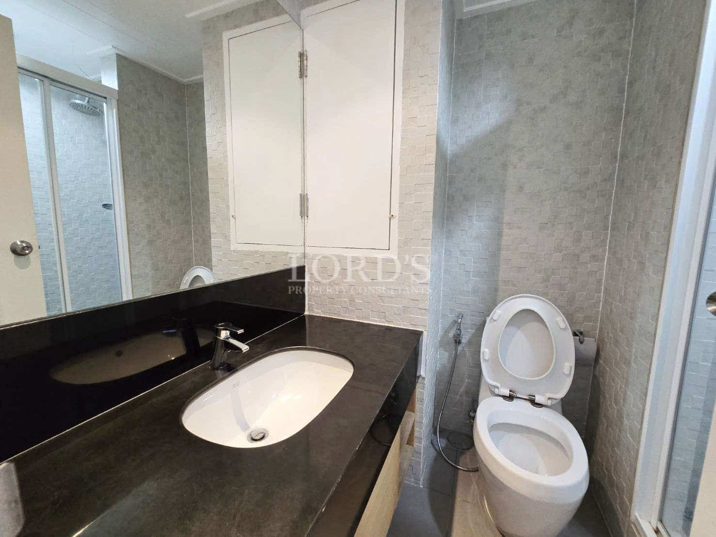 Modern bathroom with black stone vanity, white sink, toilet, and glass shower enclosure.