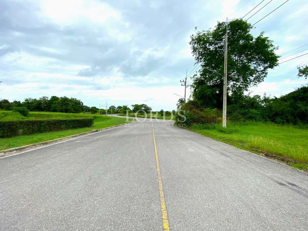 Wide paved road surrounded by green landscapes and trees under a cloudy sky.