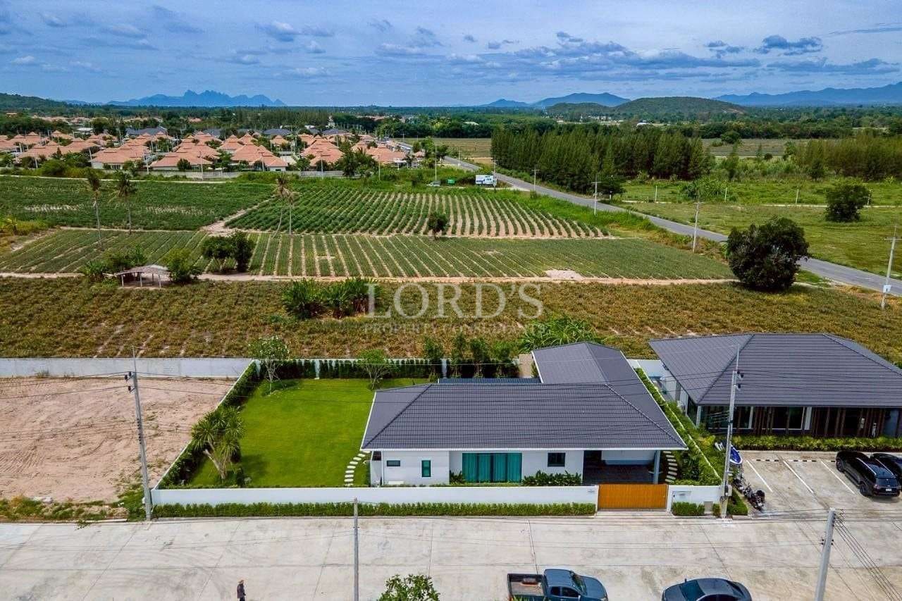 Aerial view of a modern single-story villa surrounded by farmland, greenery, and distant mountains.