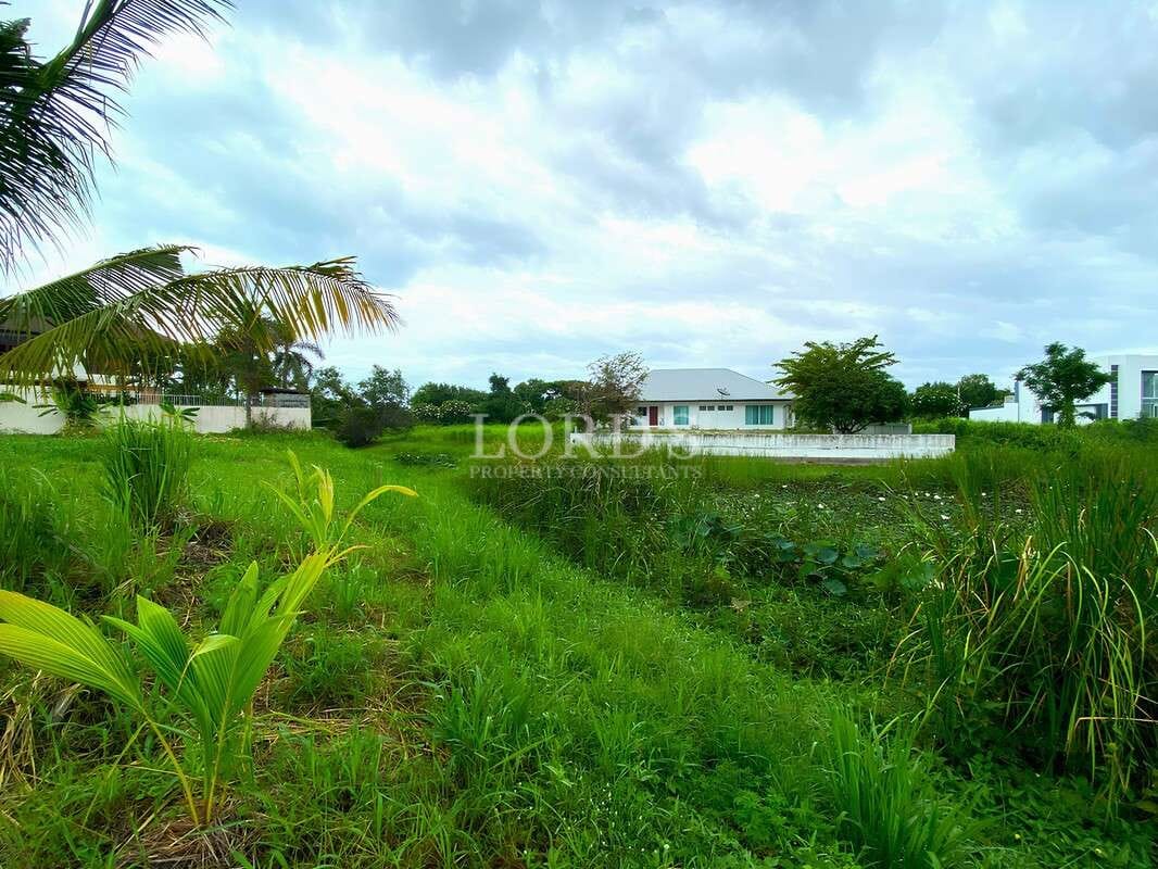 Green landscaped open area with villas in the background under a cloudy sky.