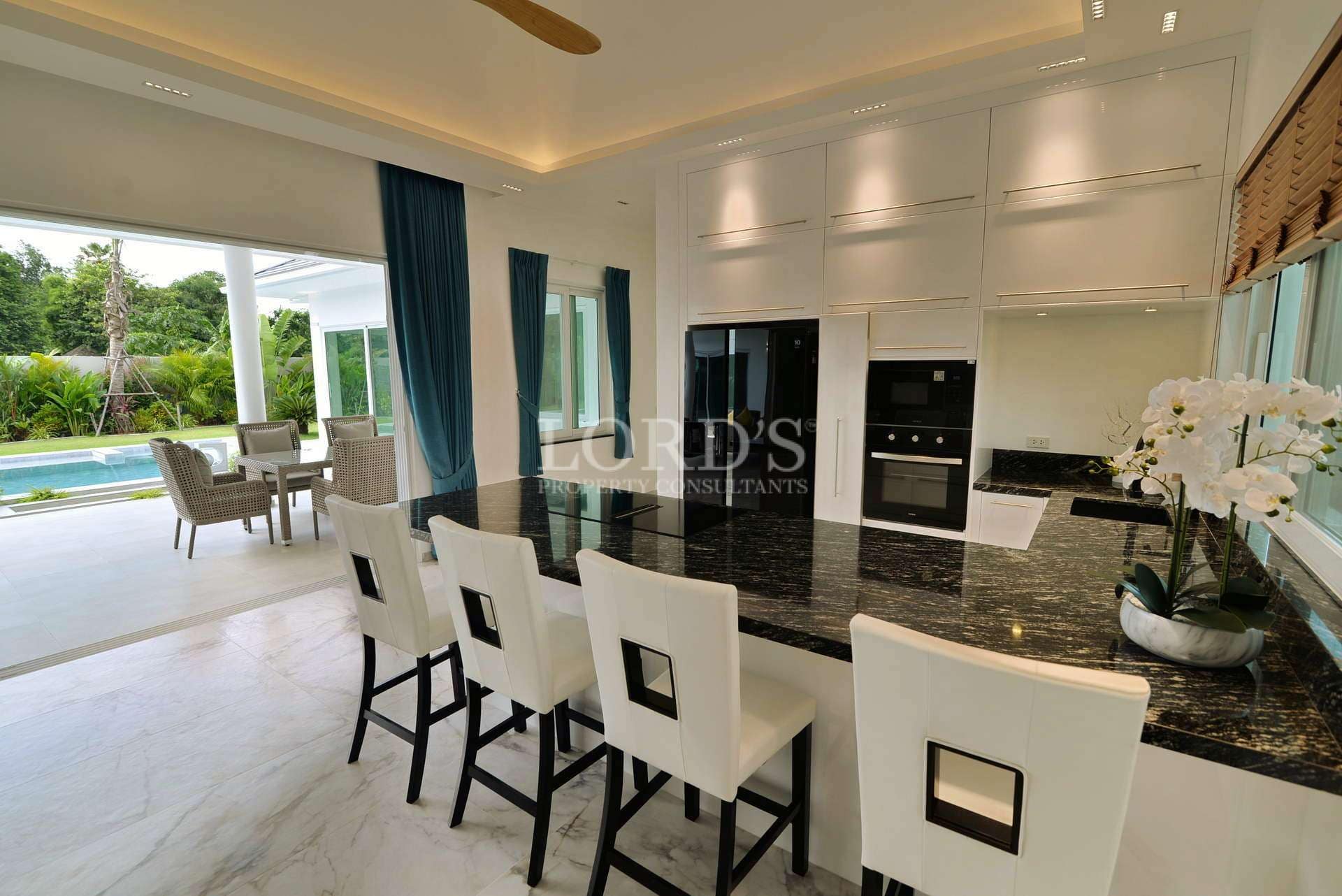 Modern open kitchen with black marble island, bar seating, built-in appliances, and poolside view.