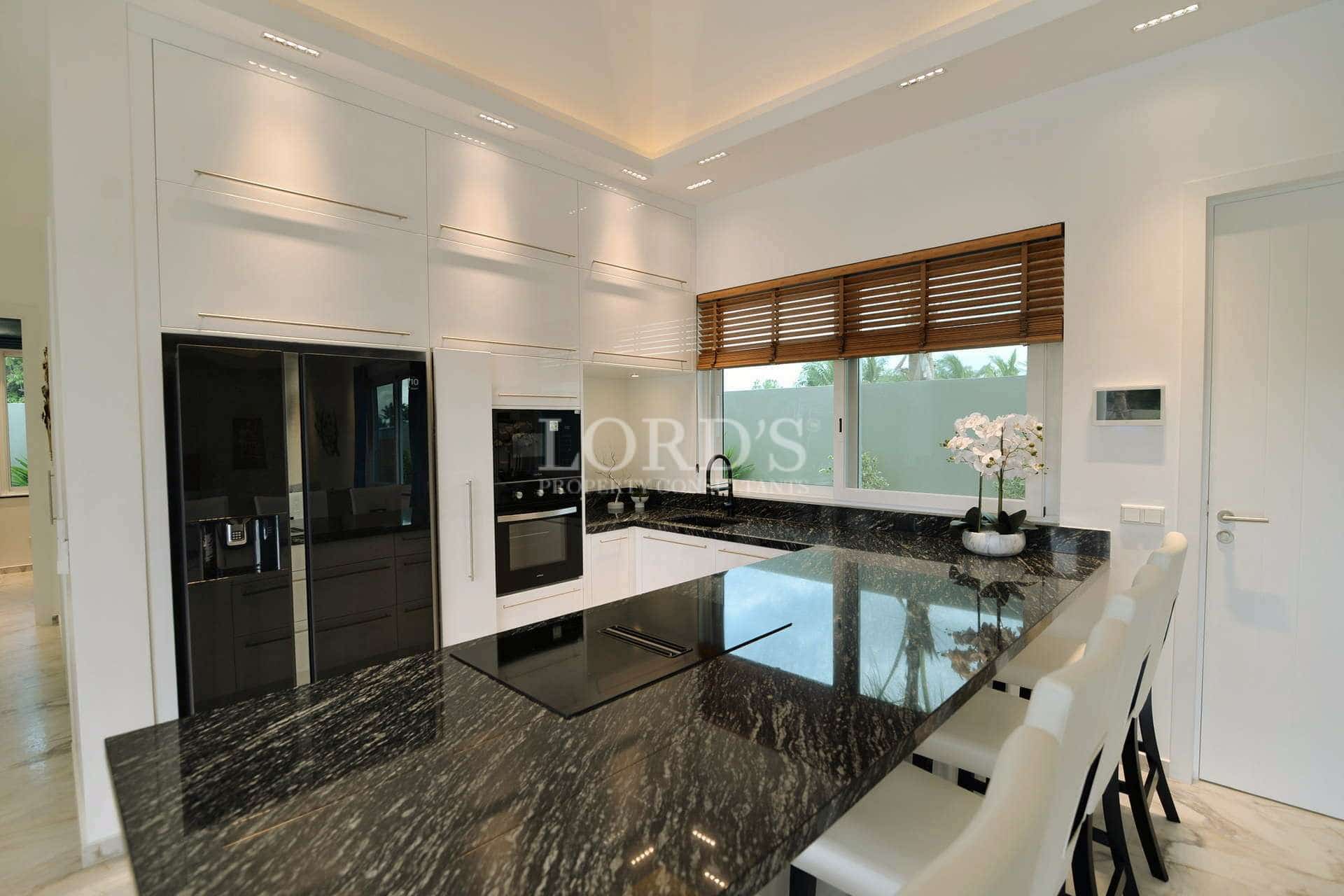 Modern white kitchen with black granite island, built-in appliances, and bar seating.