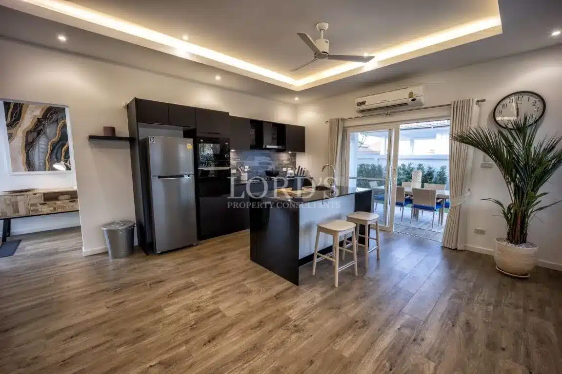 Modern open-plan kitchen with black cabinetry, island seating, wood flooring, LED ceiling lights, and patio access.