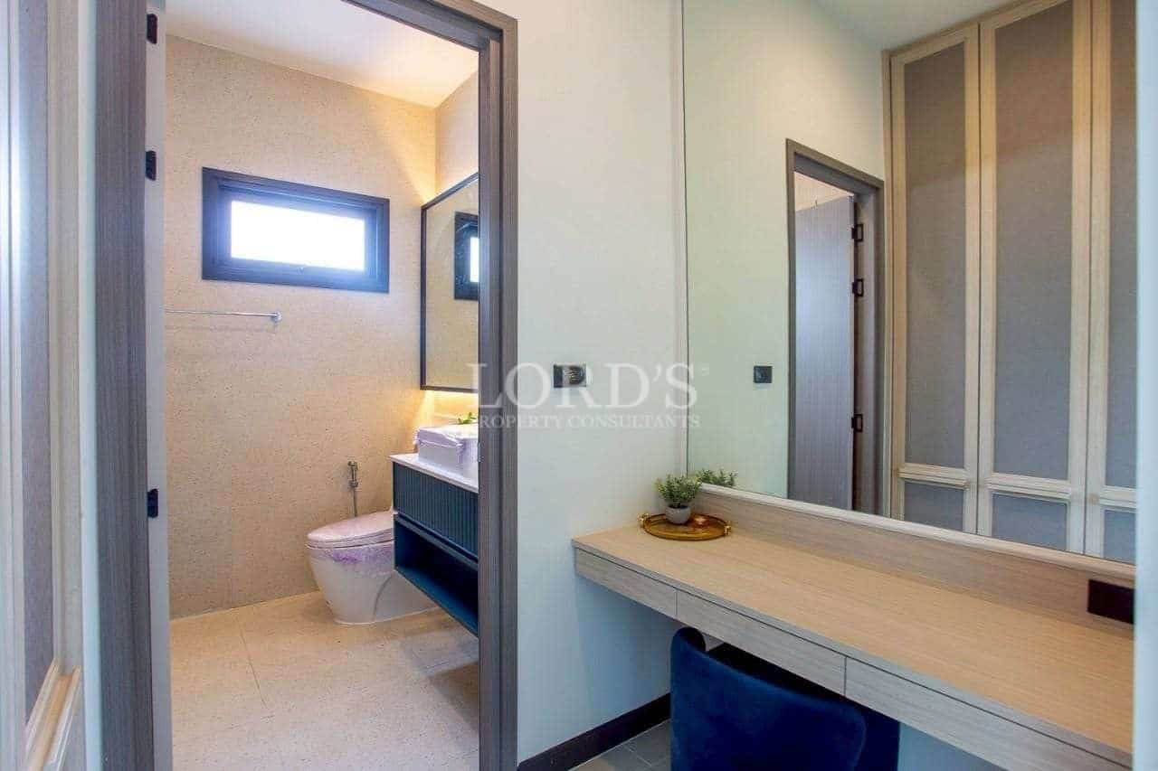 Modern dressing area with built-in vanity desk, mirror, and adjacent minimalist bathroom.
