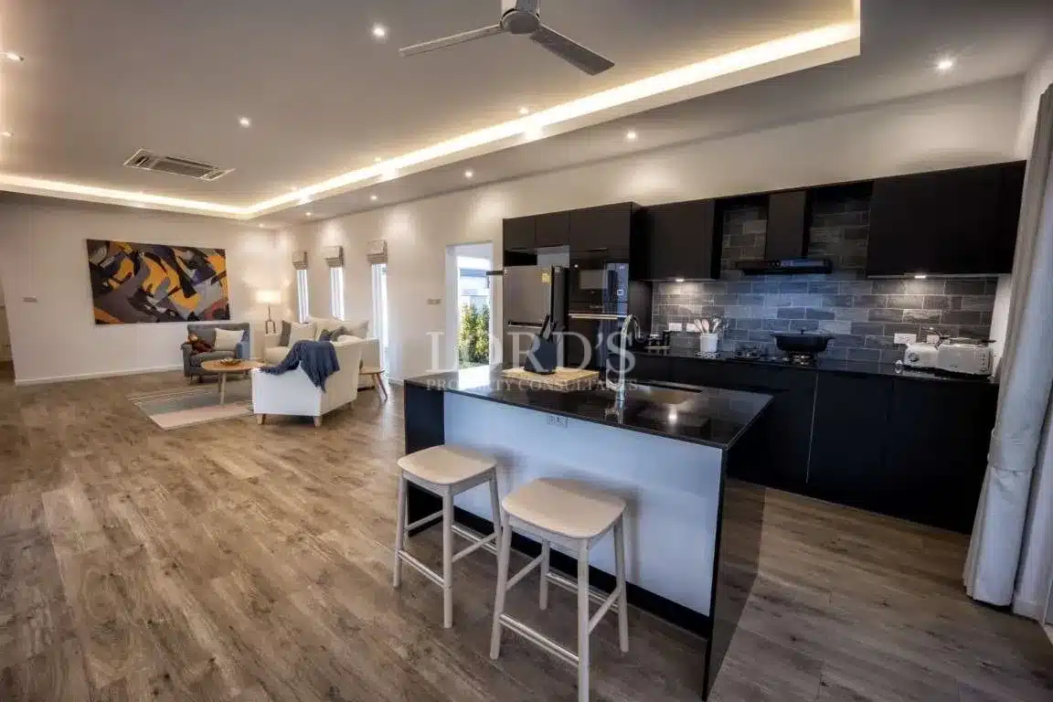 Open-plan living area with modern black kitchen, island seating, LED ceiling lighting, and stylish lounge space.