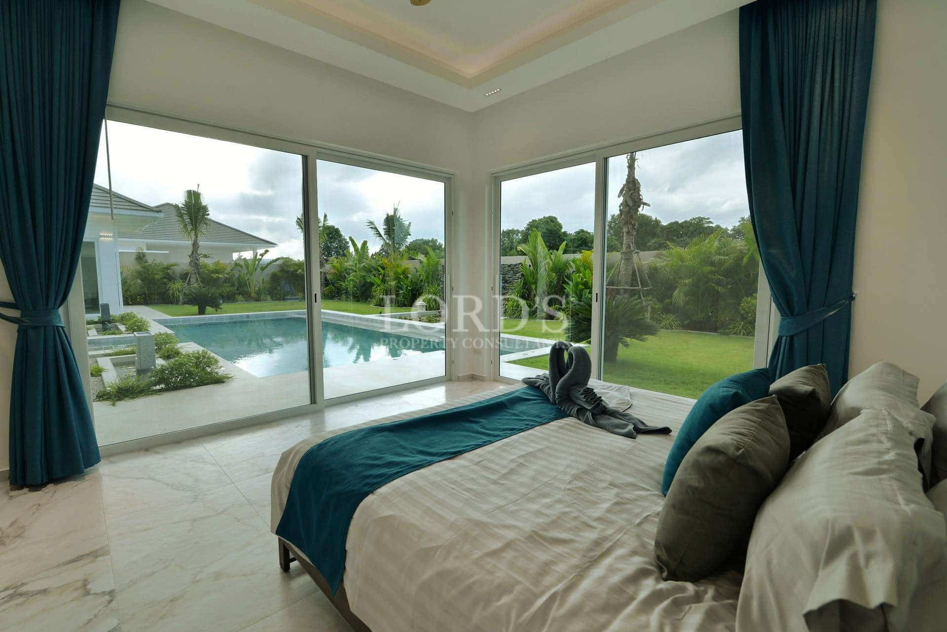 Luxury bedroom with floor-to-ceiling glass doors, pool view, marble flooring, and elegant blue accents.