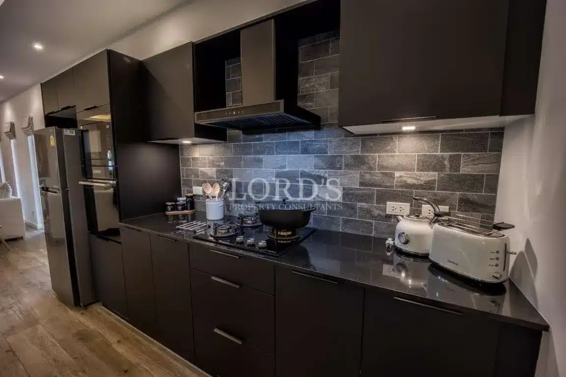 Modern black kitchen with matte cabinets, stone tile backsplash, built-in gas stove, and stainless steel appliances.
