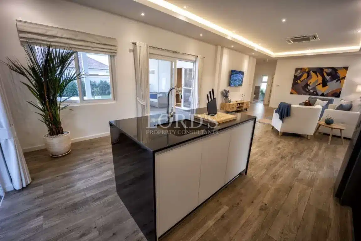 Modern open-plan kitchen with sleek island, black countertop, wood flooring, and living area in the background.