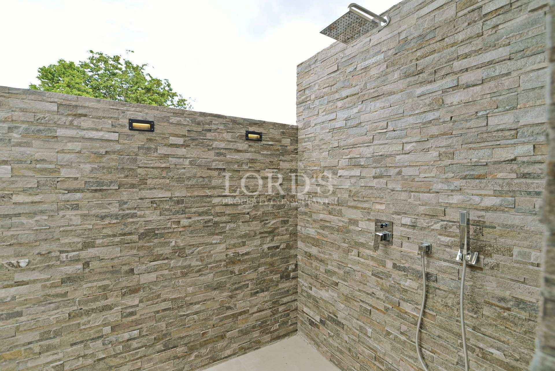 Outdoor stone shower with rain showerhead, natural stone walls, and modern fixtures in a private garden setting.