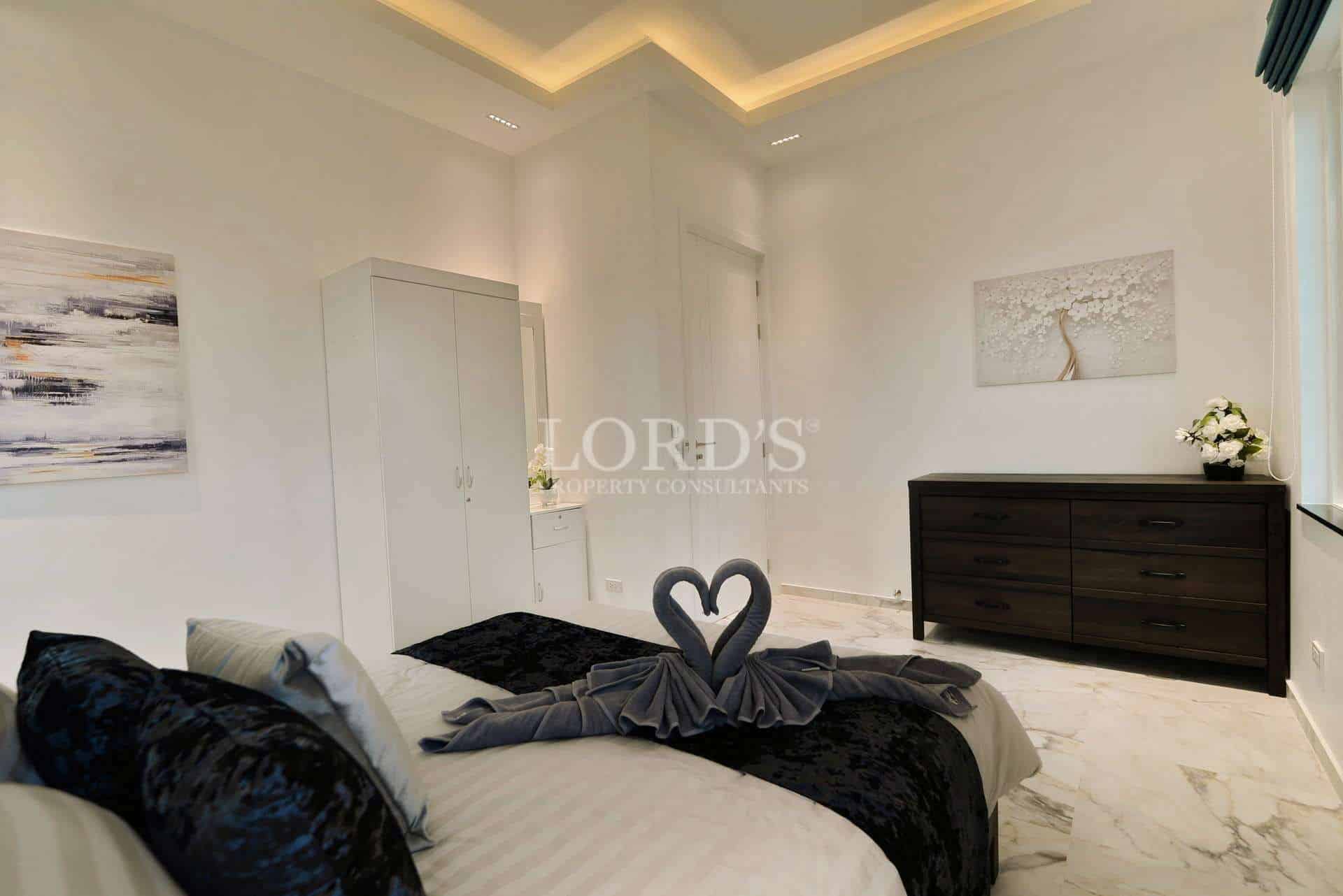 Elegant modern bedroom with marble flooring, soft lighting, minimalist furniture, and decorative towel art.