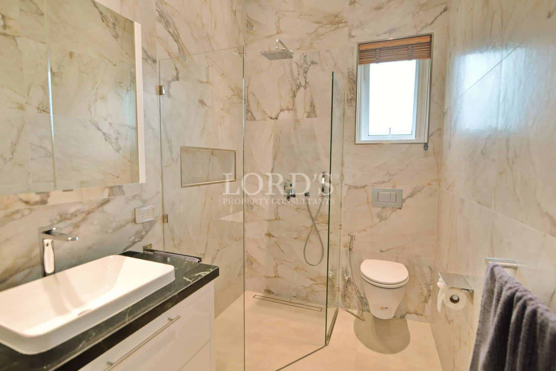 Modern bathroom with marble walls, glass shower enclosure, wall-mounted toilet, and sleek vanity.