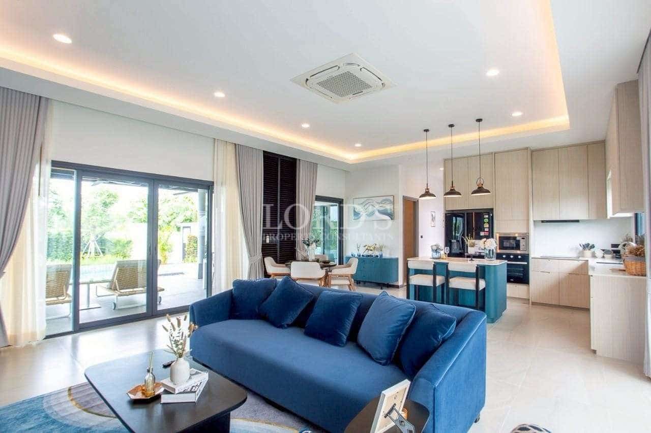 Spacious open-plan living room with blue sofa, modern kitchen island, and floor-to-ceiling sliding glass doors.