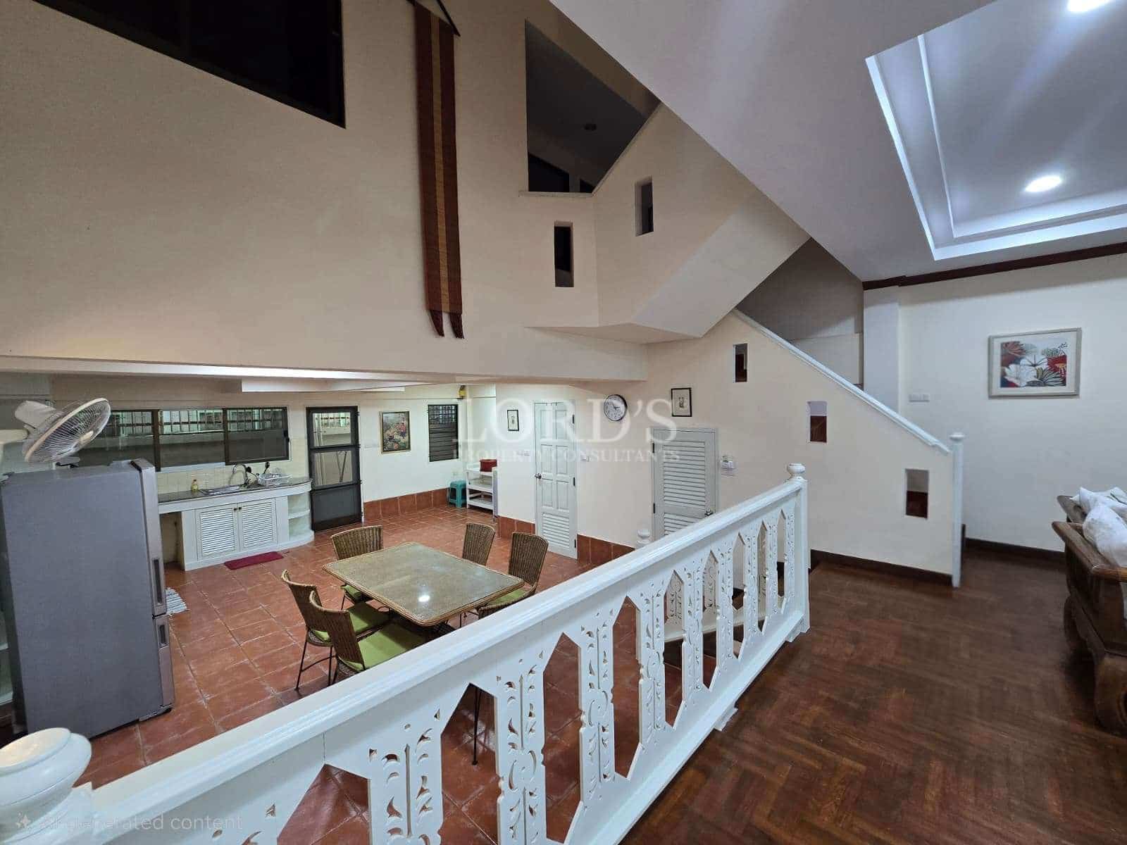 Open-plan duplex interior with staircase, upper balcony railing, dining area, and kitchen featuring tiled floors and high ceilings