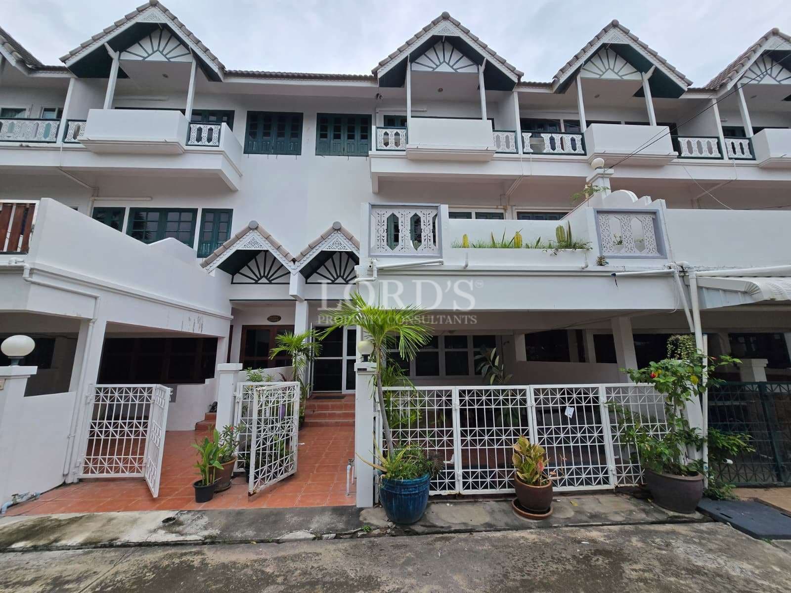 Front exterior of a multi-level townhouse with balconies, white facade, and gated entrance.
