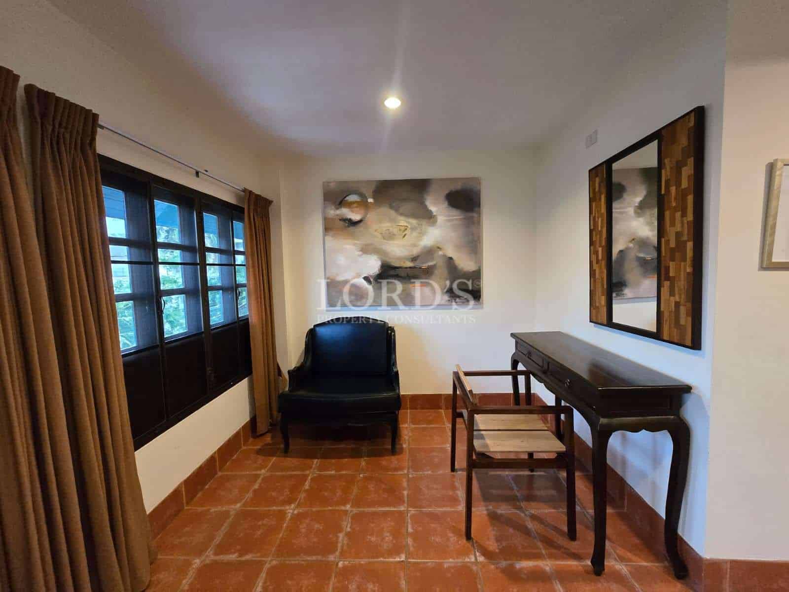 Cozy study room with wooden desk, accent chair, terracotta tile flooring, framed artwork, and soft ambient lighting.