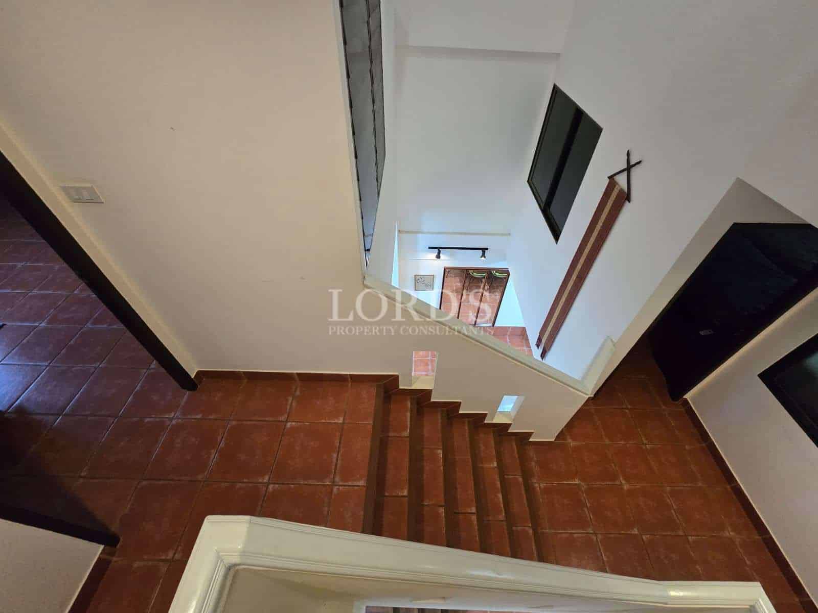 Interior stairway with terracotta tile steps and white walls connecting two floors.