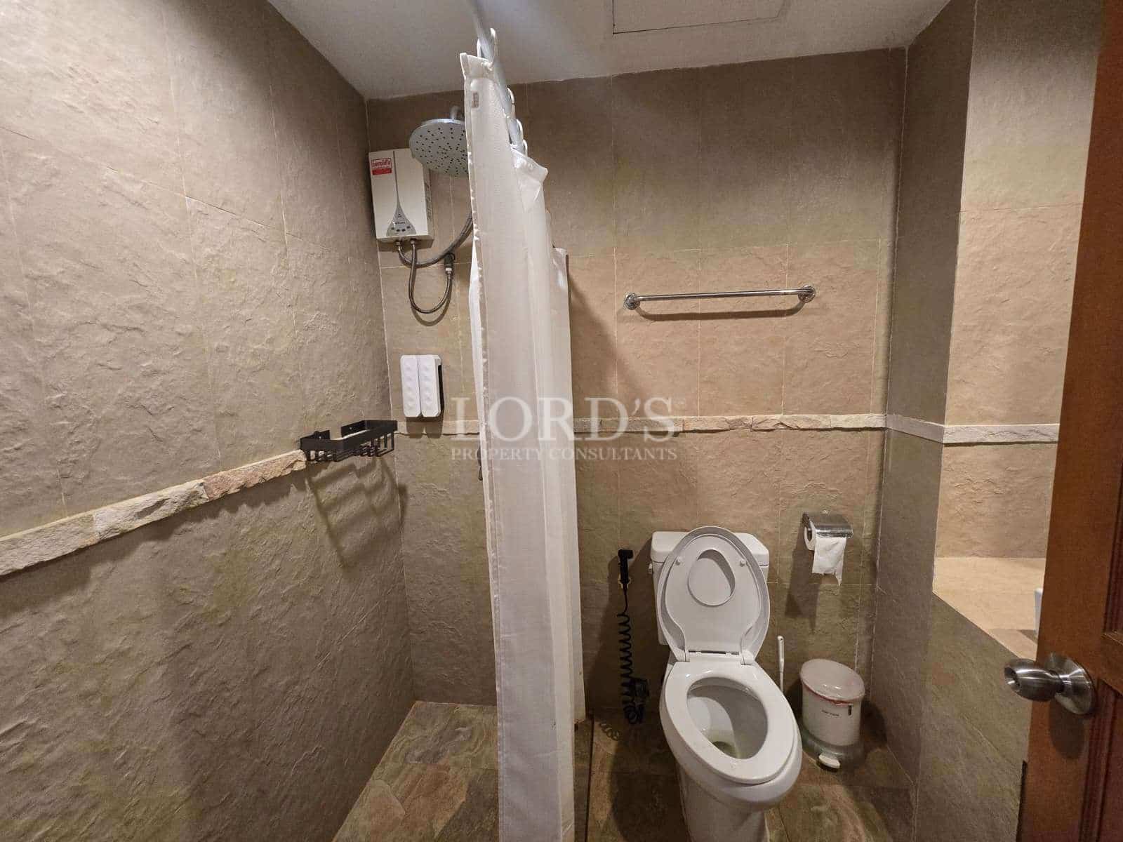 Bathroom with walk-in shower, electric water heater, toilet, and textured stone-style wall tiles.