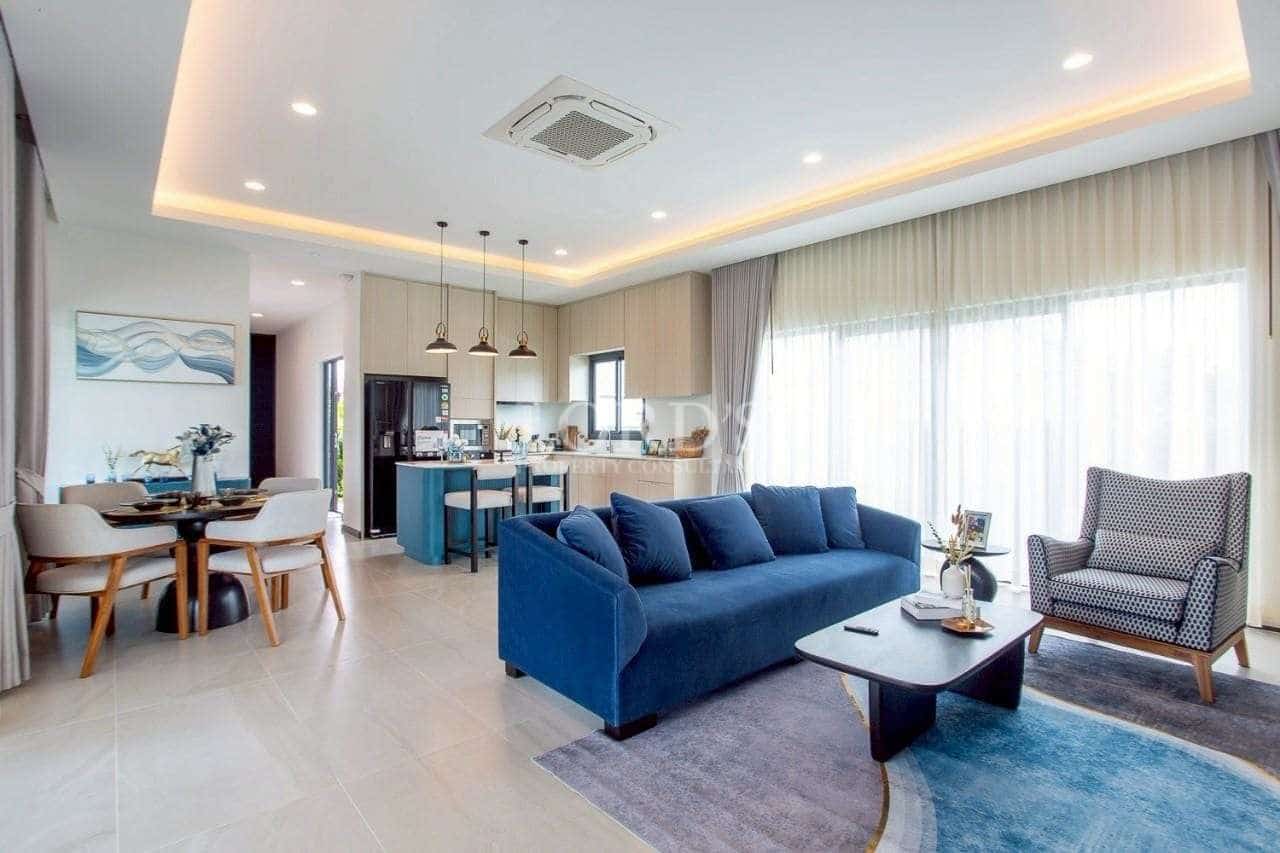 Modern open-plan living room with blue sofa, dining area, and contemporary kitchen with pendant lighting.