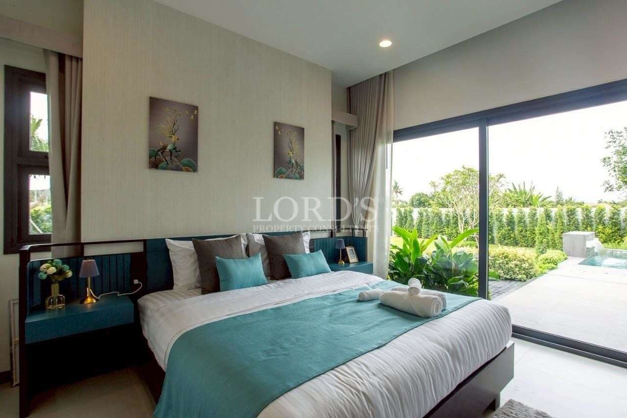 Elegant bedroom with teal bedding and floor-to-ceiling glass doors overlooking a private garden.