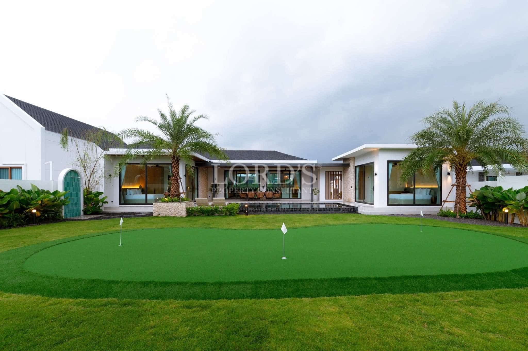 Luxury modern villa with a private putting green, palm trees, landscaped lawn, and contemporary single-story design.