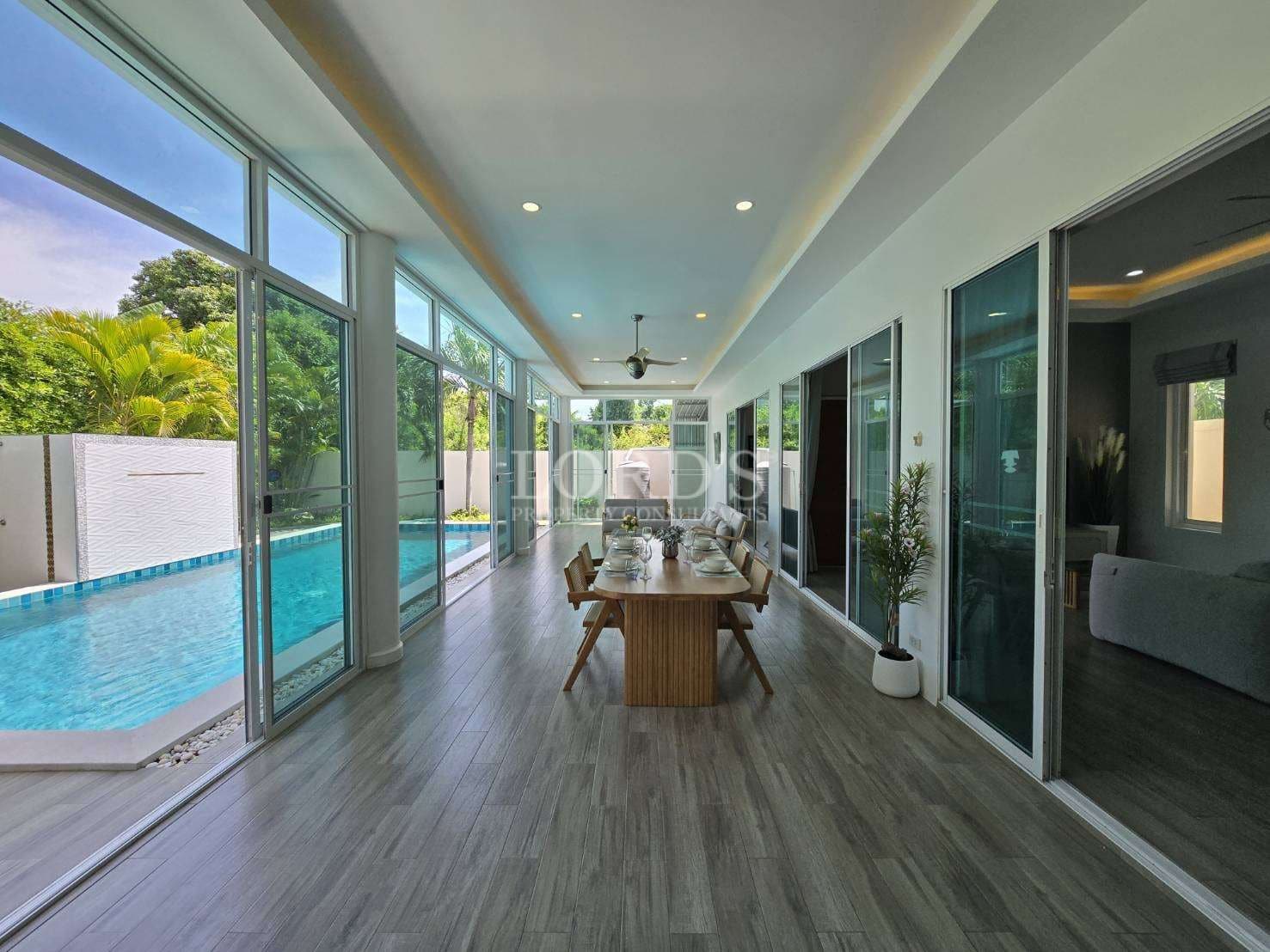 Covered outdoor dining area with floor-to-ceiling glass doors beside a swimming pool.