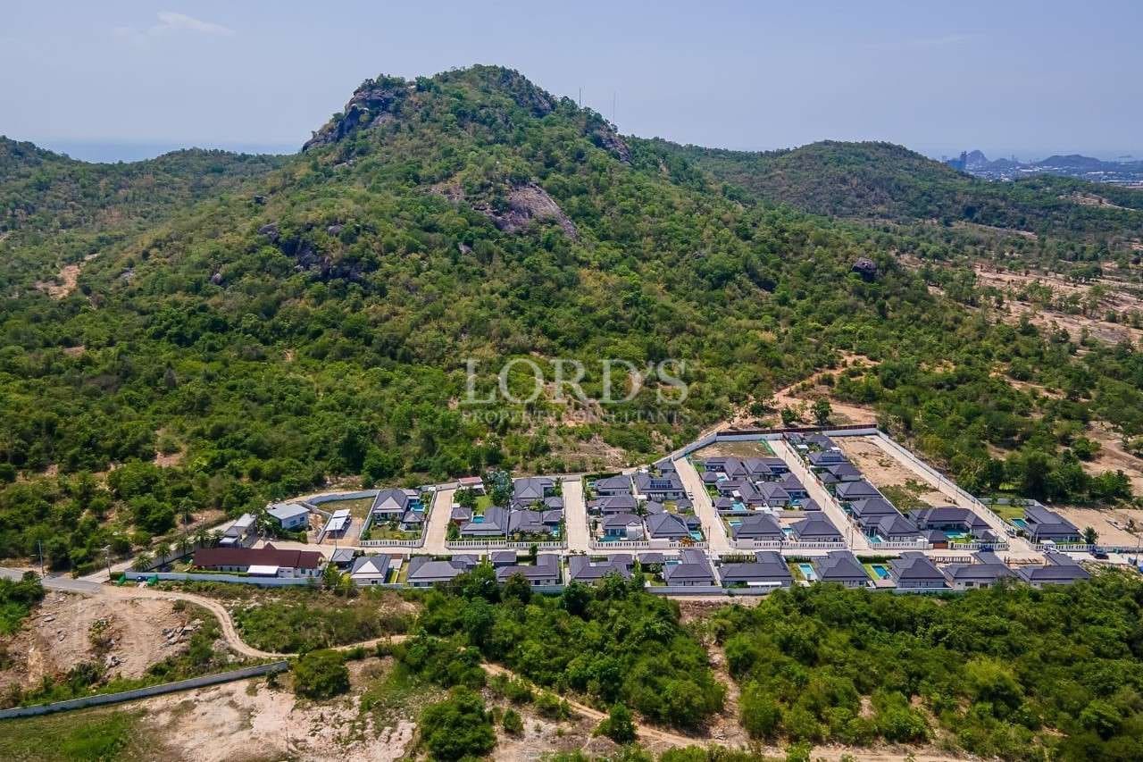 Aerial view of a residential villa community surrounded by lush green hills.