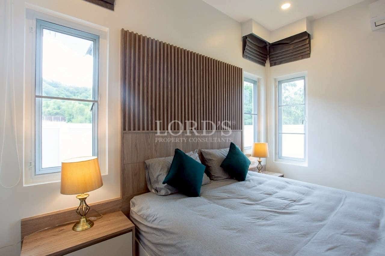 Modern bedroom with wooden accent headboard, large windows, and warm bedside lighting.