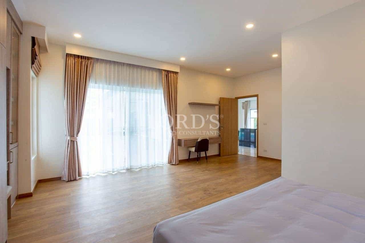 Spacious modern bedroom with wooden flooring, work desk, and floor-to-ceiling glass doors.