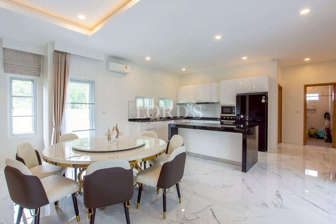 Bright open-plan dining area with modern kitchen, marble flooring, and built-in appliances.