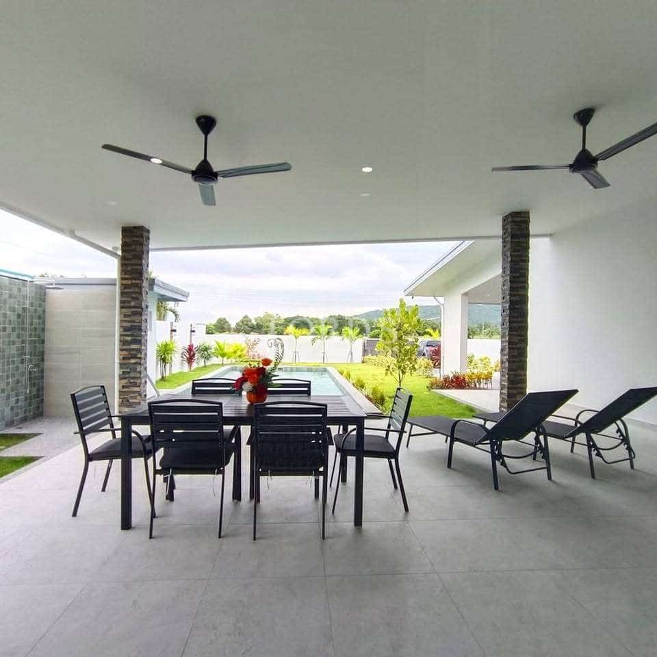 Covered outdoor patio with ceiling fans, dining table, lounge chairs, and a view of a private swimming pool and landscaped garden.