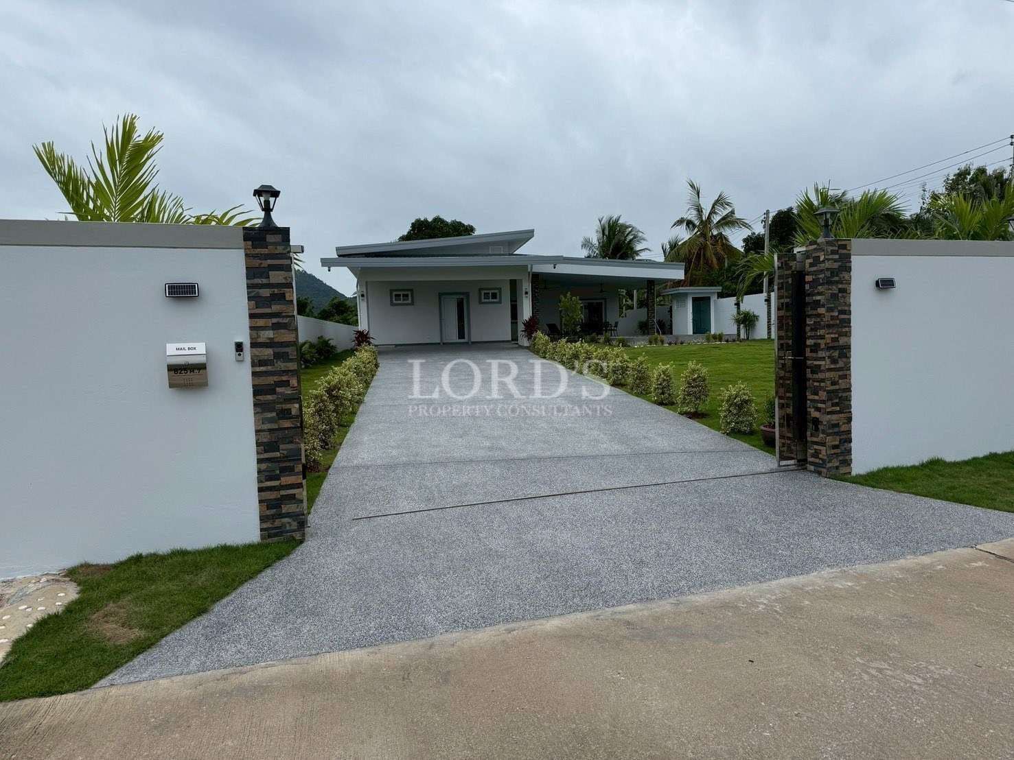 Modern villa entrance with gated driveway, landscaped lawn, stone-accent walls, and contemporary single-story home.