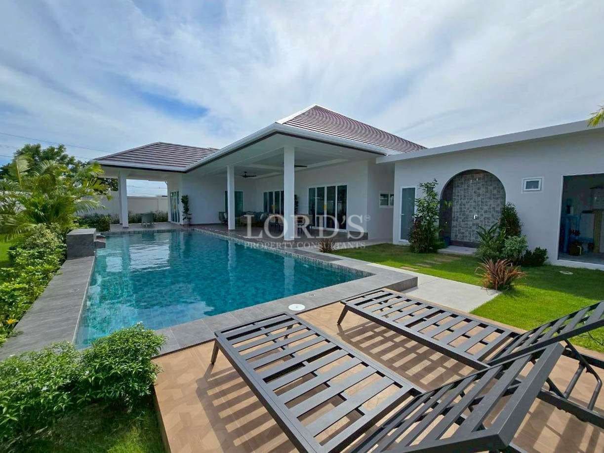 Private swimming pool with sun loungers, covered terrace, and landscaped garden in a modern villa.